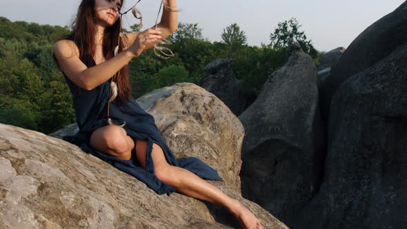 Ancient Woman Sits on Edge of Cliff Looks Feathers Woven Into Hair