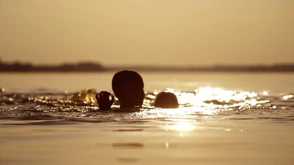 Silhouette of two cute boys in water background. Children swimming in the river