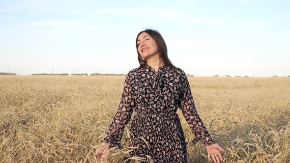 Young Woman Walks in a Dress on a Field of Ripe Wheat and Smiles