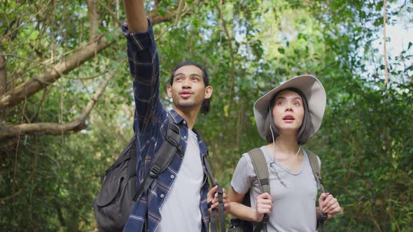 Asian man and woman friend travel and walk in the forest with smile during summer holiday vacation.