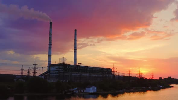 Factory chimneys smoke on the river bank in the evening