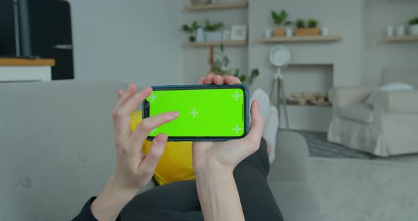 Young Woman at Home Lying on a Couch Using with Green Mock-up Screen Smartphone in Horizontal