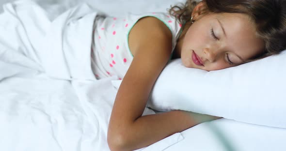 Little girl sleeping on a big and cozy bed white linen