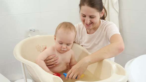 Happy Smiling Mother and Baby Boy Playing with Toy Boats and Ships in Small Plastic Bath