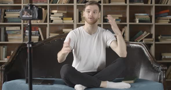 Positive Millennial Blogger Recording Video About Literature in Library. Portrait of Young Handsome