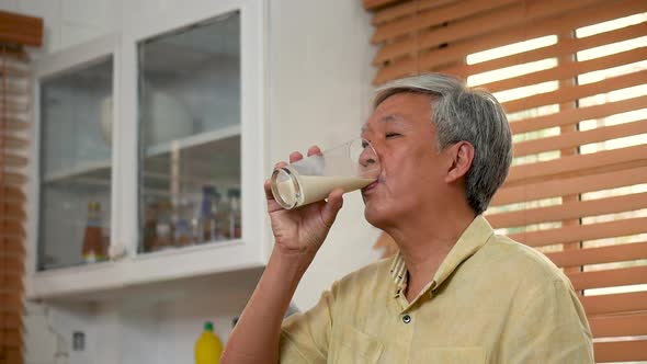 Portrait senior Asian man drinking milk in kitchen at home.