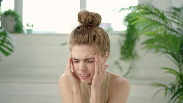 Young Brunette Woman with Bun on Her Head is Experiencing Severe Headaches