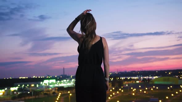 Rear View Young Woman Enjoying Amazing View of Modern Night City Standing on Rooftop