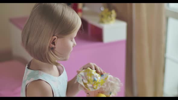 Side View Close-up of Caucasian Girl's Face Looking at Camera and Signing As Playing with Her Doll