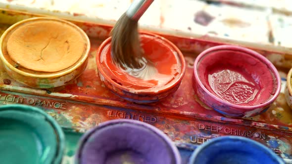 Artists watercolor palette messy with yellow, orange, red and purple paint