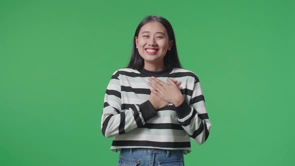 Proud Asian Woman Touching Her Chest While Standing In Front Of Green Screen Background