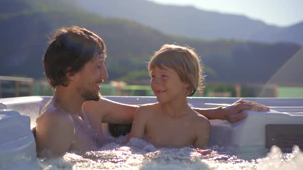 A Young Man and His Son Relaxing in the Hot Tub on a Rooftop with a View on Mountains