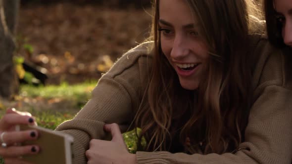 Twin teenage girls lying in the grass as they look at smartphone