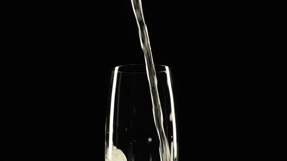 Foamy Sparkling Yellow Water is Pouring Into Wineglass Standing on Black Background in Slowmotion