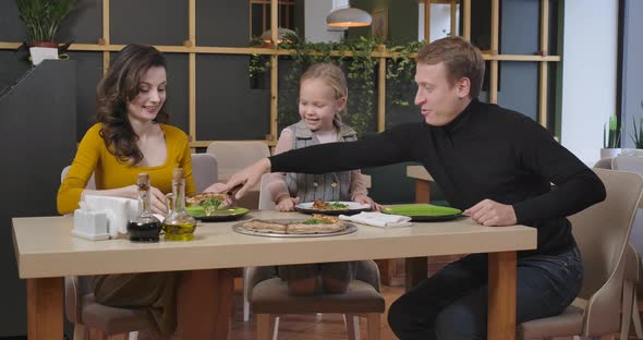 Cheerful Man Putting Pizza on Plates of Family in Restaurant