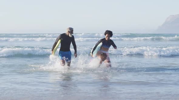 Happy african american couple running with surfboards on sunny beach