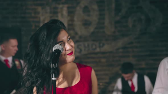 Pretty Female Vocalist Sings Into Microphone on Stage with Musical Group