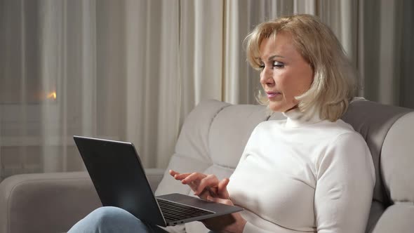 Woman of Middle Age Works Using Laptop and Sitting on Sofa