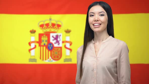 Smiling Asian Woman Showing Thumbs-Up Gesture Against Spanish Flag Background