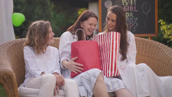 Happy Surprised Pregnant Mother Sitting with Daughters on Couch on Backyard Talking Smiling