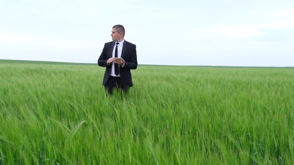 Young Businessman in a Suit Walking on a Wheat Field with a Tablet in His Hands