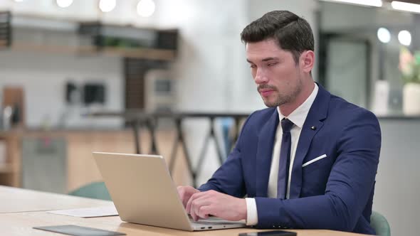 Cheerful Businessman with Laptop Smiling at Camera in Office 