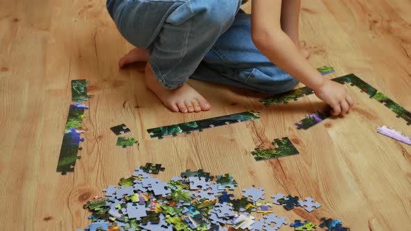 A Beautiful Little Girl Assembles a Complex Puzzle on a Wooden Floor