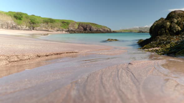 Close up shot of water steadily flowing across a beach and into a turquoise ocean, eroding the sand