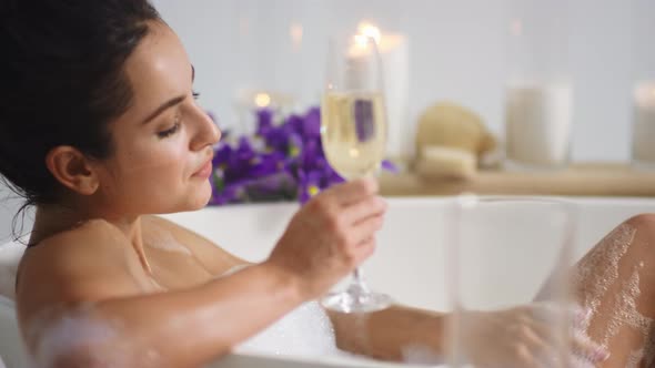 Sexy Woman Washing Legs with Foam in Bath. Girl Drinking Champagne in Bathtub
