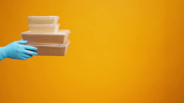 People's Hands Passing Each Other Packed Boxes with Food Delivery Against Yellow Studio Background