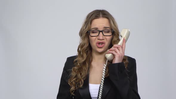 Portrait of Angry Businesswoman Shouting in White Phone on Gray Background.