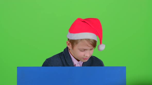 Teenager in a Red Hat Appears From a Board on a Green Screen