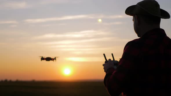 Silhouette of a Farmer Using a Drone in a Wheat Field at Sunset. Concept Technology Innovations