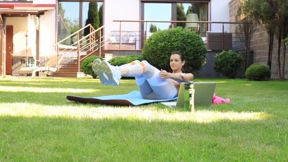 Attractive slim girl in sportswear is doing abs exercise outdoor. Healthy lifestyle.