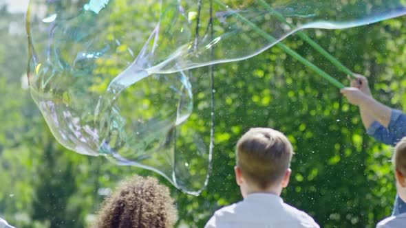 Man Launching Giant Bubble Up in the Air at Kids Party alt