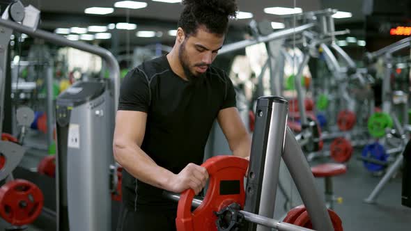 Athletic Bodybuilder Man Trains in Gym with Barbell Lifting Adding Weights