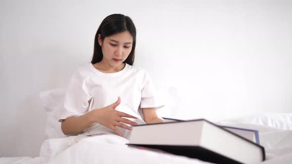 Asian young woman reading a book on the bed