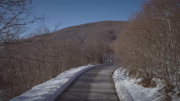 Aerial view of a snowy road with blue sky and a hill at the end.