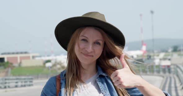 Tourist woman with hat at the airport showing thumbs up gesture.