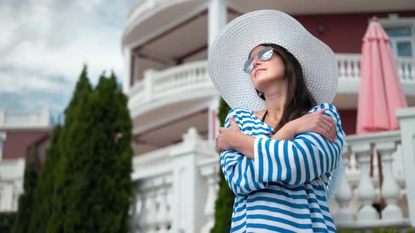 Low Angle Elegant Woman in Sunglasses and Hat Standing with Crossed Hands Smiling and Enjoying