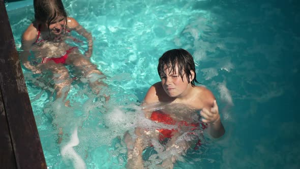 High Angle View of Proud Confident Little Boy and Girl Sitting in Bubbling Water in Swimming Pool in