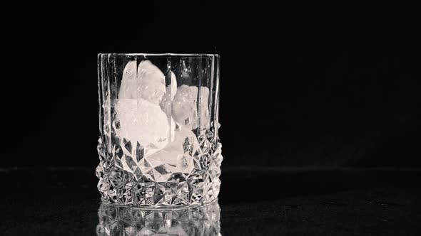 Dropping Ice Cubes. Whiskey Being Poured Into A Glass on Black Background. Close Up.