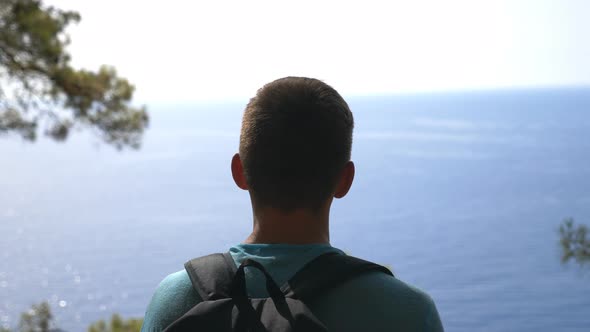 Male Hiker with Backpack Standing on Edge Hill and Admiring Beautiful Seascape. Man Enjoying Travel