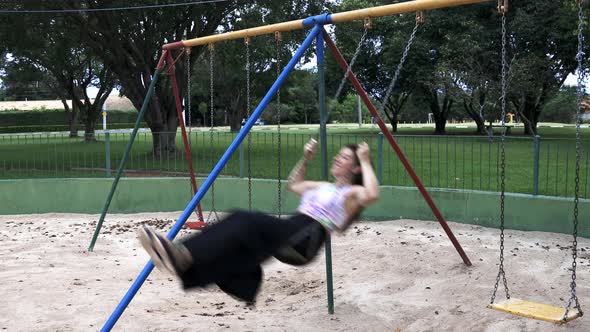 young woman with long skirt and colorful shirt swinging and laughing feeling free and happy at a par