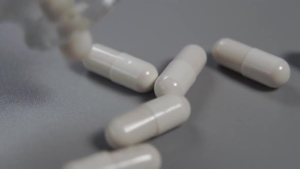 Close-up white capsules spill out of a glass bottle onto a gray plastic surface