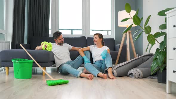 Tired Couple Sits on the Floor in a Room and High Five Each Other After They Finish Cleaning the