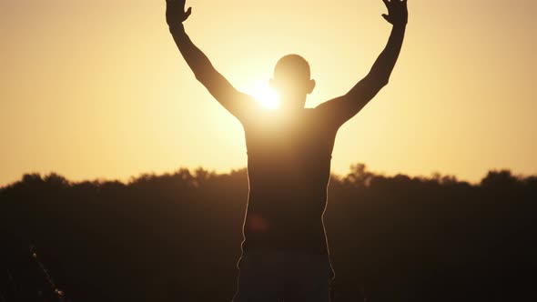 Silhouette of Young Man Against Sunset Raising Hands Sides and Up. Slow Motion