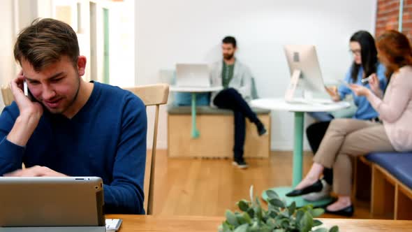 Male executive talking on mobile phone while using digital tablet