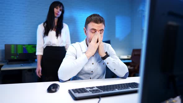 Exhausted Man Rubbing Face As Nervous Woman Yelling and Gesturing at Background in Blue Office