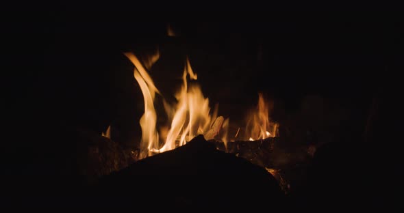 A warm campfire is burning bright at night with the silhouette of rocks in front of it.